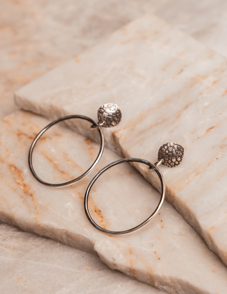 Organic-style silver hoop earrings with artisan embossing and handcrafted charm