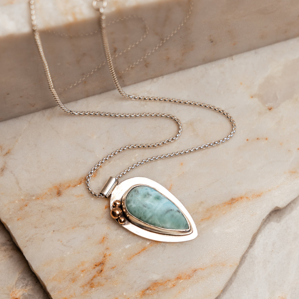 The Delta Necklace, a statement piece perfect for any occasion, featuring a larimar gemstone and sterling silver with 14k gold accents.