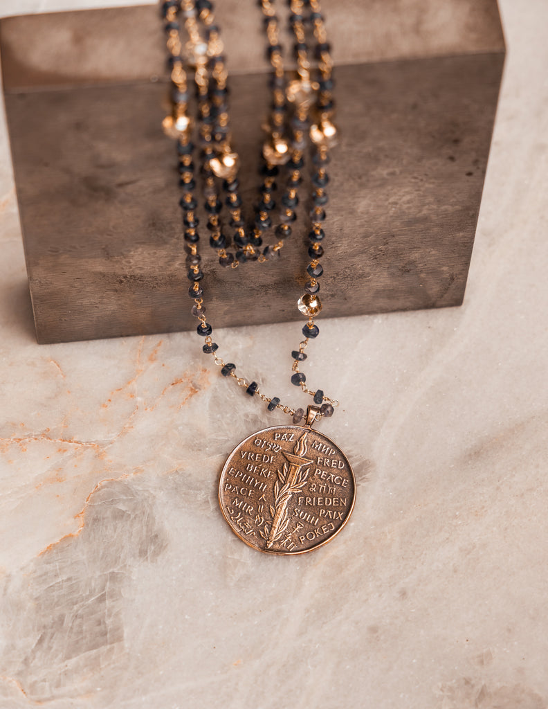 Artisan statement necklace – iolite gemstone strands with bronze peace pendant.