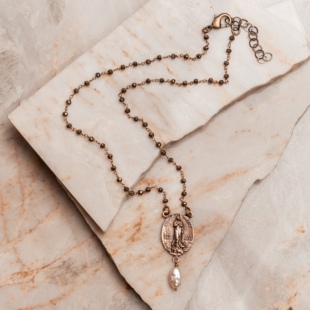 Faith-inspired artisan necklace featuring a hand-cast bronze Virgin Mary pendant and elegant keshi pearl charm on a pyrite beaded chain.